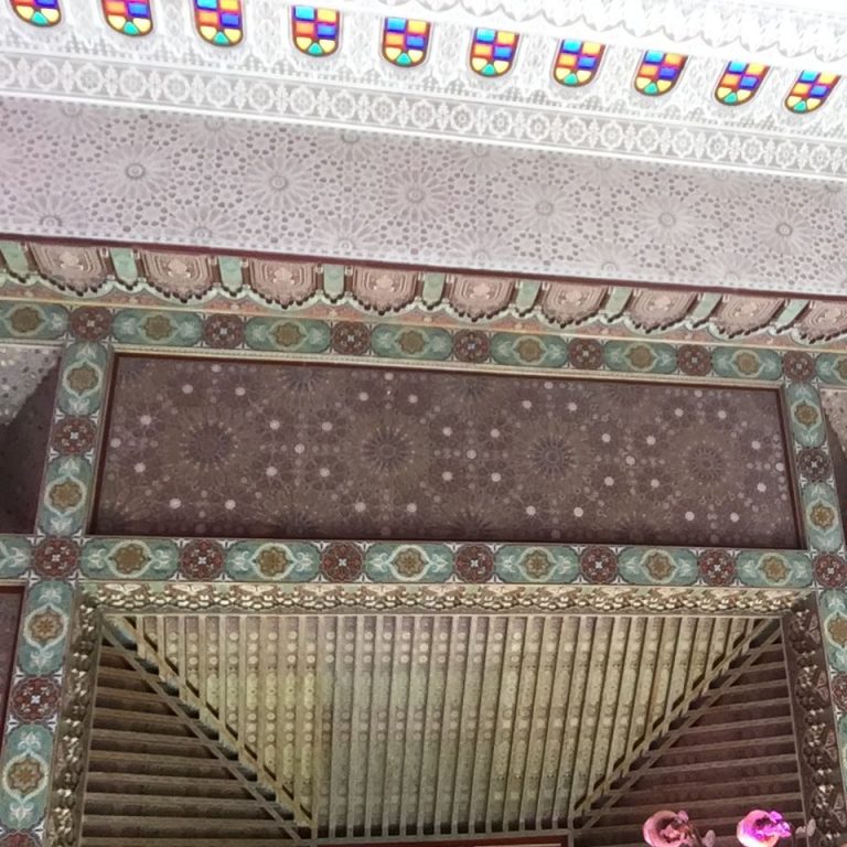 A hand holding a glass of drink in front of waterfalls and a teapot in the background.