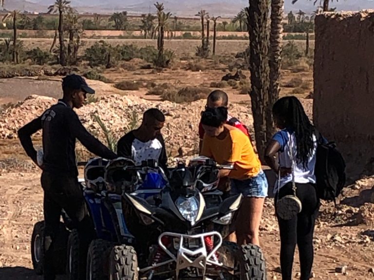 Five people gathered around an ATV in a desert setting, discussing something.