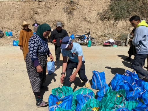 People collecting supplies from blue bags in a rural outdoor setting.