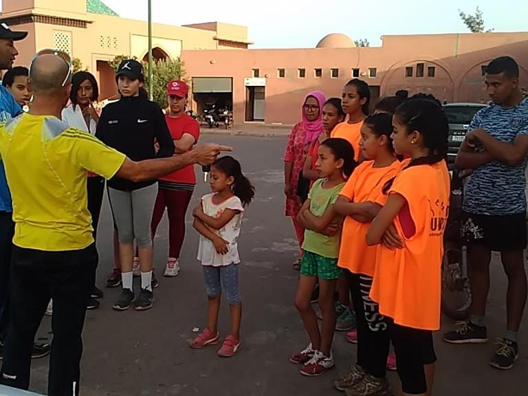 Group of children in bright shirts listening to an adult in a discussion.