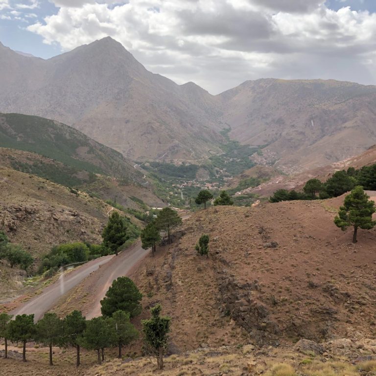 Scenic mountainous valley with winding road and sparse trees under a cloudy sky.