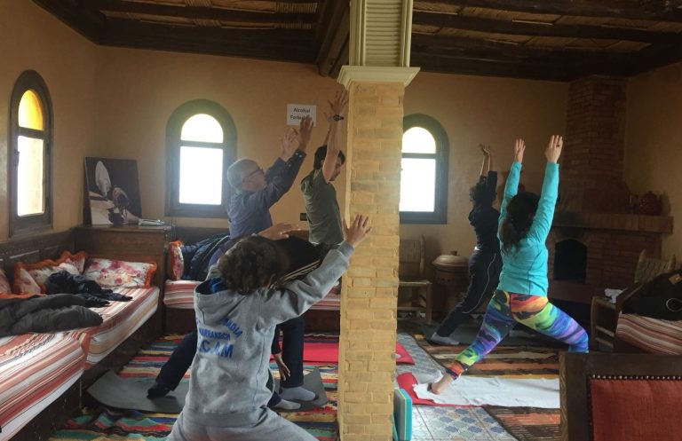 A line of people on camels trekking through a sandy landscape.