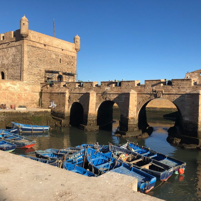 Two boats at a dock, one with a person sorting supplies, surrounded by blue tarps.