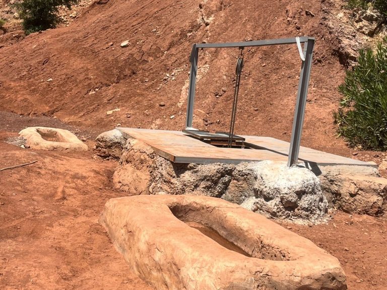 A metal swing set on a rocky surface near two stone troughs.