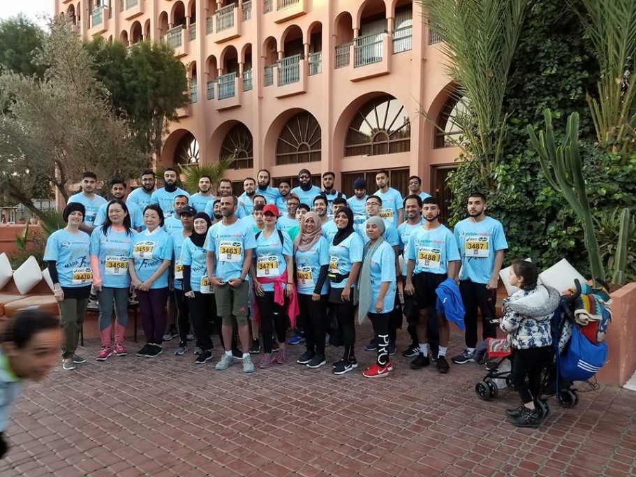 Group of children in matching blue t-shirts posing outdoors in front of a building.