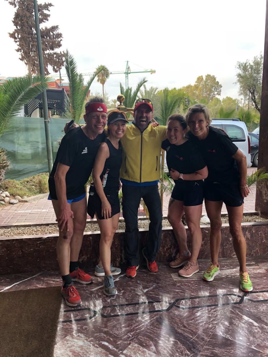 Five people standing together, all smiling, outdoors with palm trees in the background.