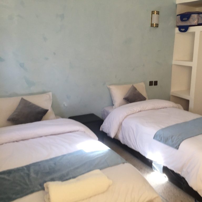 Two twin beds with light bedding in a simple, pastel-coloured room.