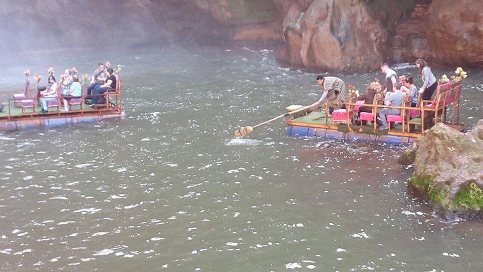 Two rafts with people float on a misty river surrounded by rocky cliffs.