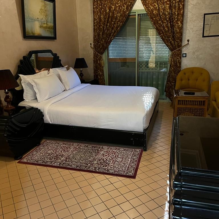 A comfortable hotel room featuring a double bed, armchair, and decorative curtains.