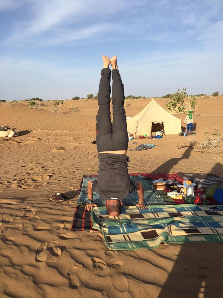 Person performing a handstand on a patterned mat in a desert campsite.