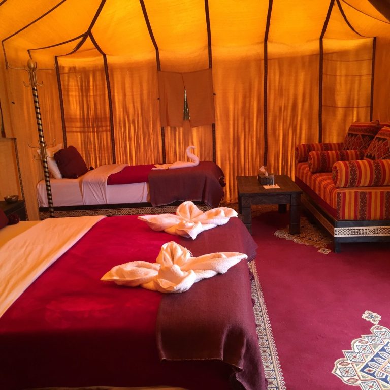 Luxurious tent interior with two beds, vibrant seating, and warm colours.