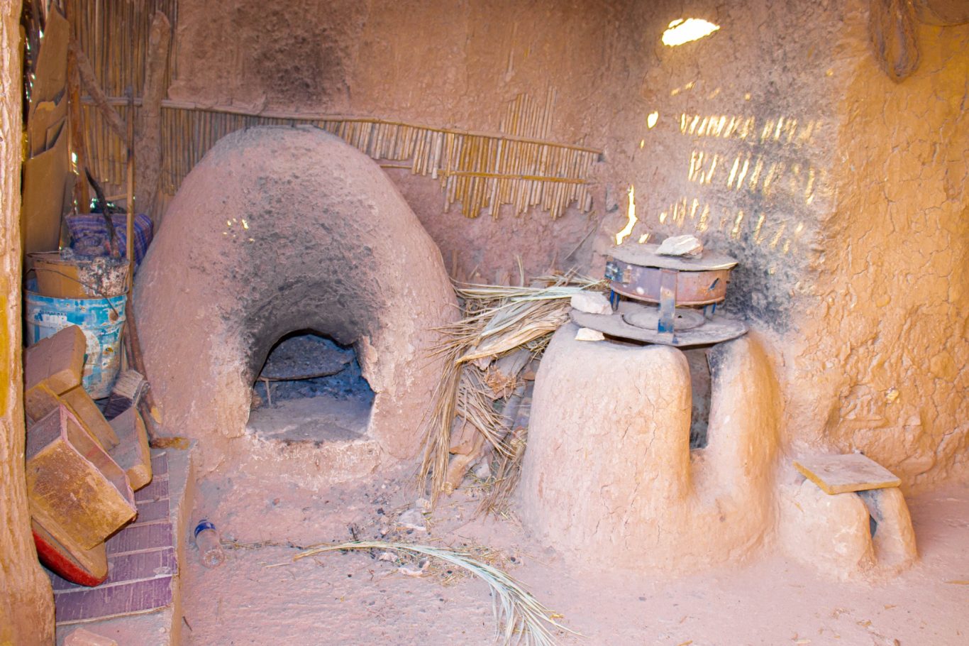Interior of a traditional earthen kitchen with a clay oven and cooking tools.