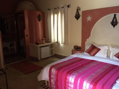 Bright bedroom with pink and white bedding, decorative walls, and soft lighting.