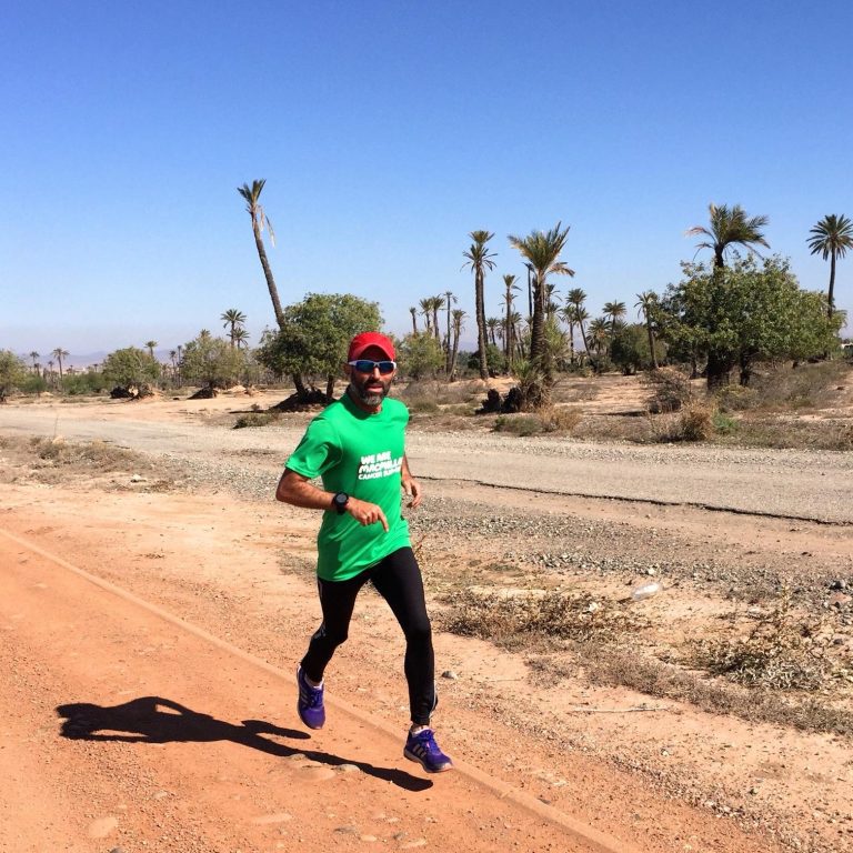 A person running on a dirt path in a desert landscape with palm trees.