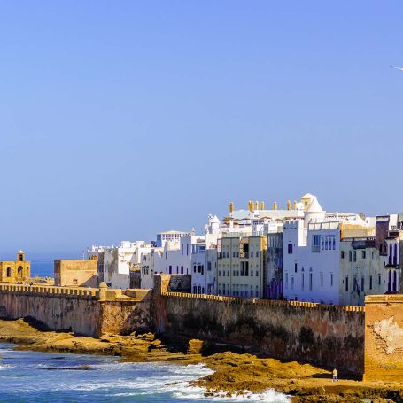 Coastal view of white buildings along a rocky shoreline under a clear blue sky.