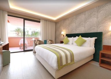 Bright hotel room featuring a king-sized bed, balcony, and modern decor.