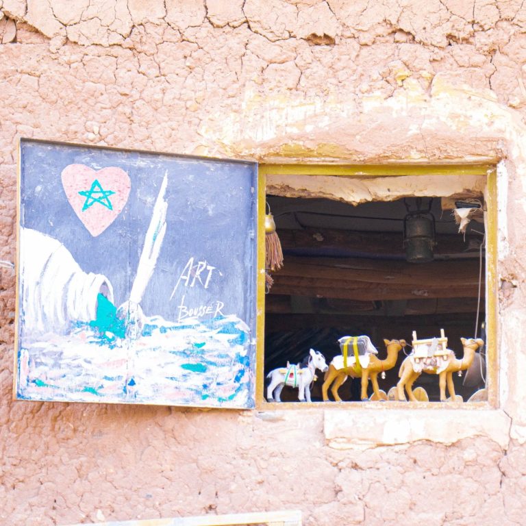 Open window with a painted scene and carved camel figurines on display.