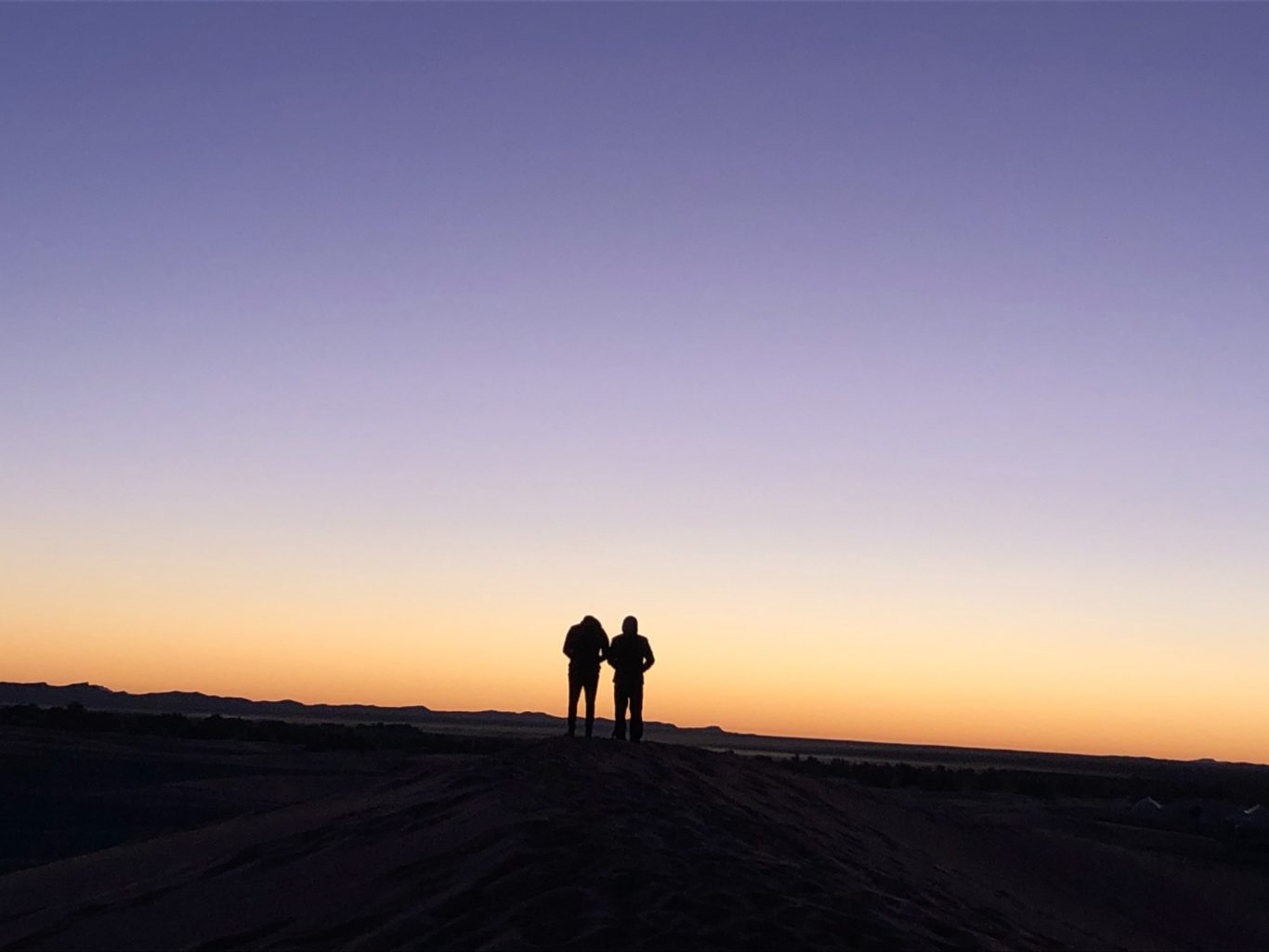 Silhouetted couple walking together against a colourful sunset sky.