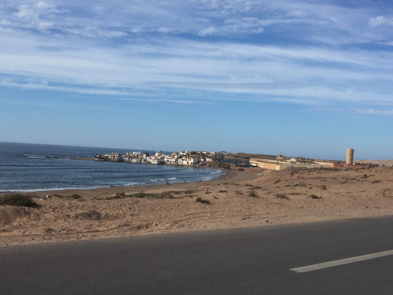 Coastal landscape with buildings along the shore under a blue sky.