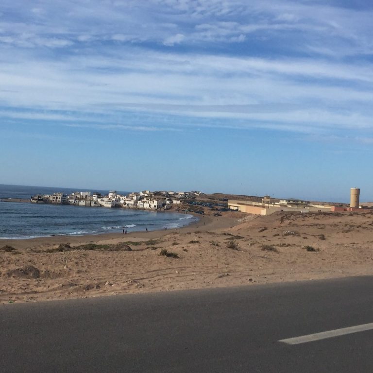 Old stone castle by a river, with blue fishing boats docked nearby.