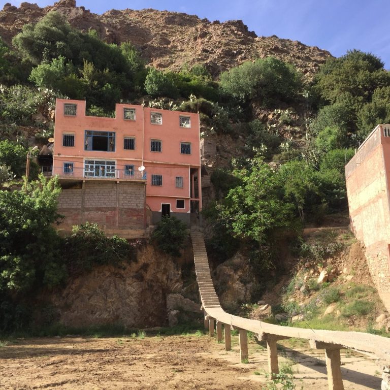 Pink house perched on a hillside, connected by a wooden walkway.