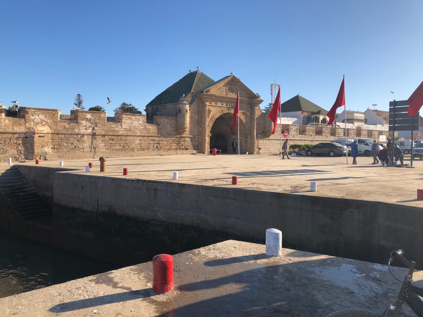Historic stone building with flags, set against a clear blue sky by the waterfront.
