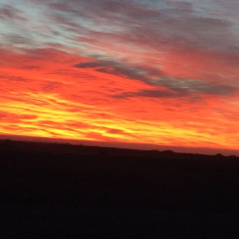 Vibrant sunset with orange and pink hues over a dark landscape.