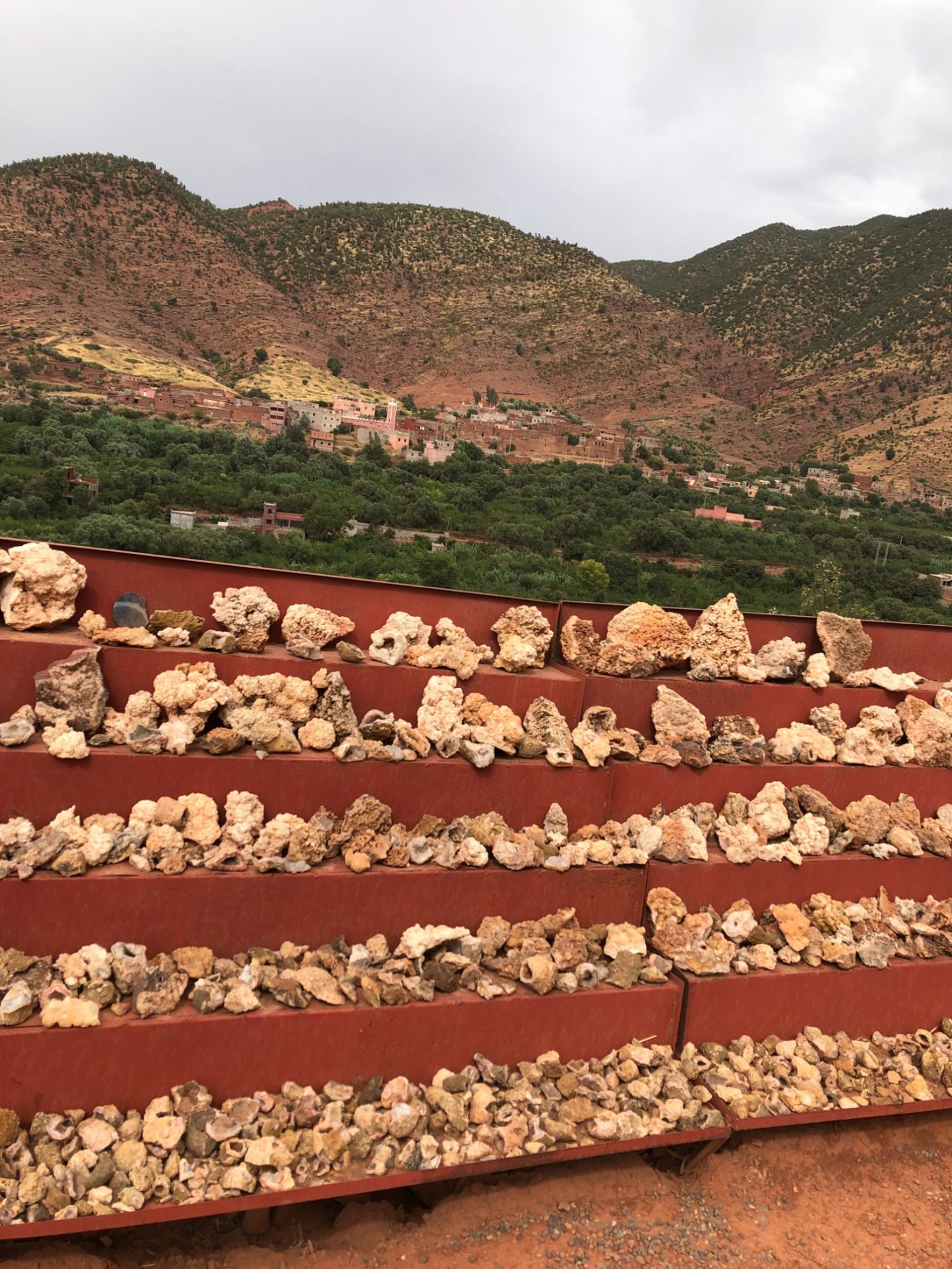 Terraced landscape with stone rows against lush green hills and cloudy sky.
