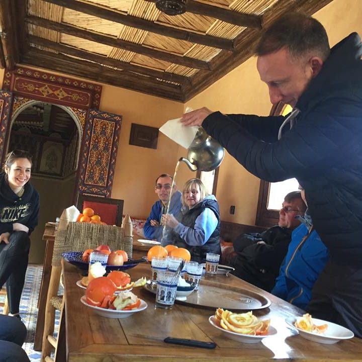 A group enjoying tea and snacks in a traditional setting with orange slices.