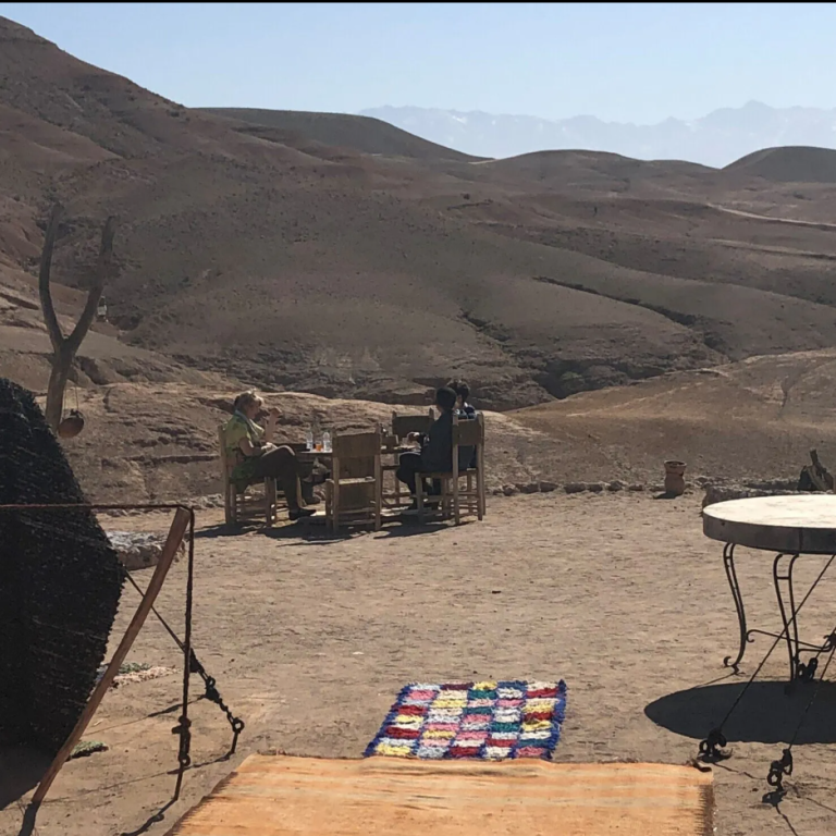 Desert landscape with mountains, a patterned rug, and wooden furniture in the background.