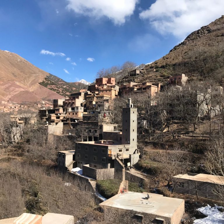 A hillside village with stone buildings, surrounded by mountains and trees.