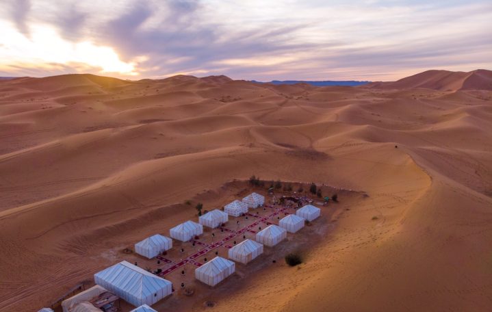 A campsite nestled among vast golden sand dunes at sunset.