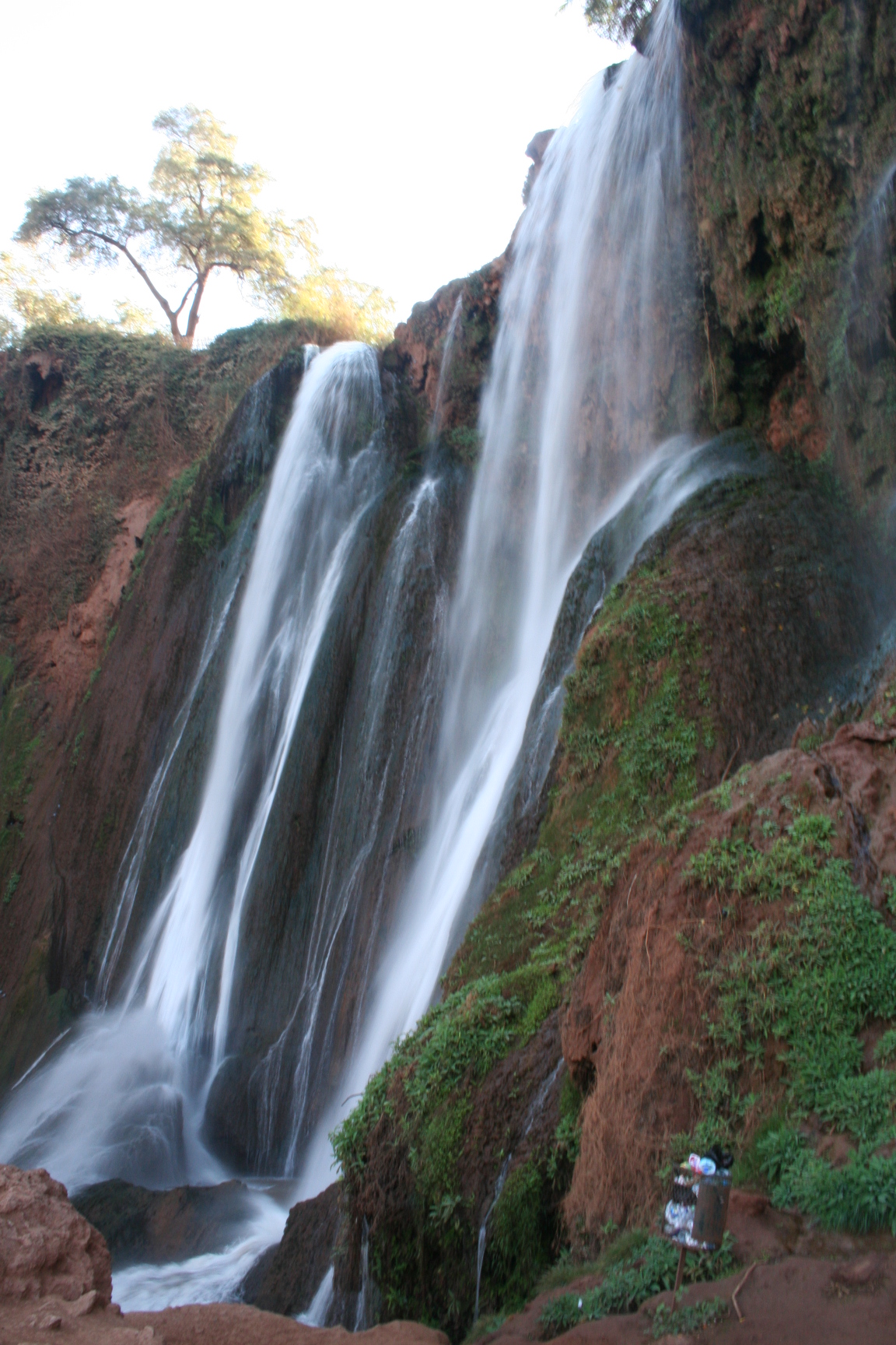 A cascading waterfall surrounded by lush greenery and rocky terrain.