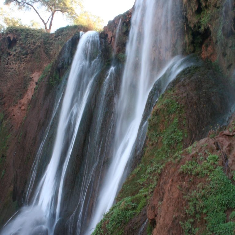 A cascading waterfall surrounded by lush greenery and rocky terrain.
