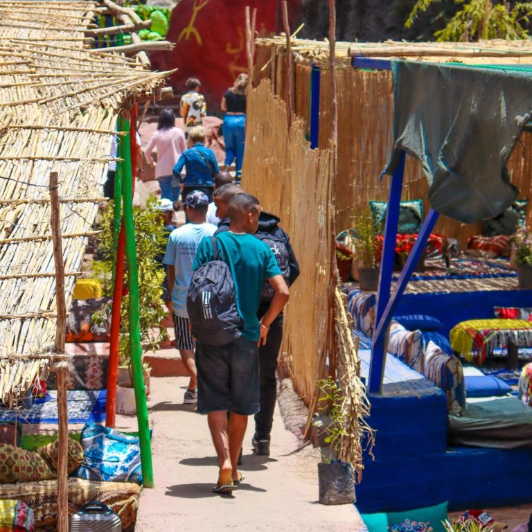 Narrow pathway through colourful market stalls, visitors walking along the vibrant surroundings.