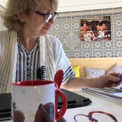 A woman with glasses studies documents at a table with a coffee mug and patterned decor.