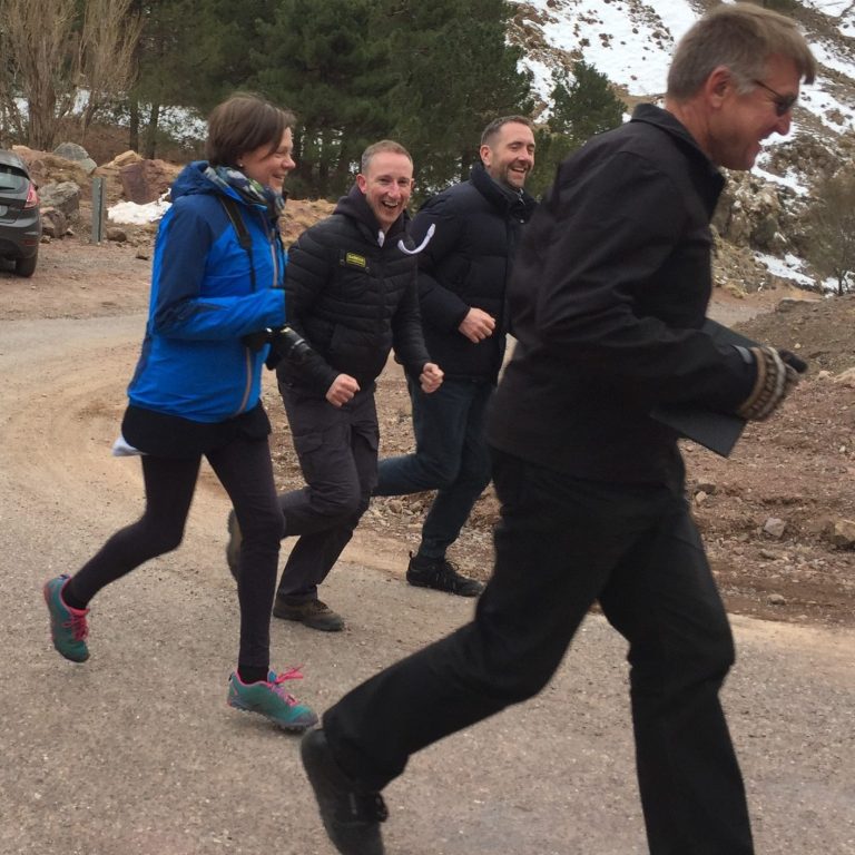 Group of four people jogging along a gravel road in a mountainous area.