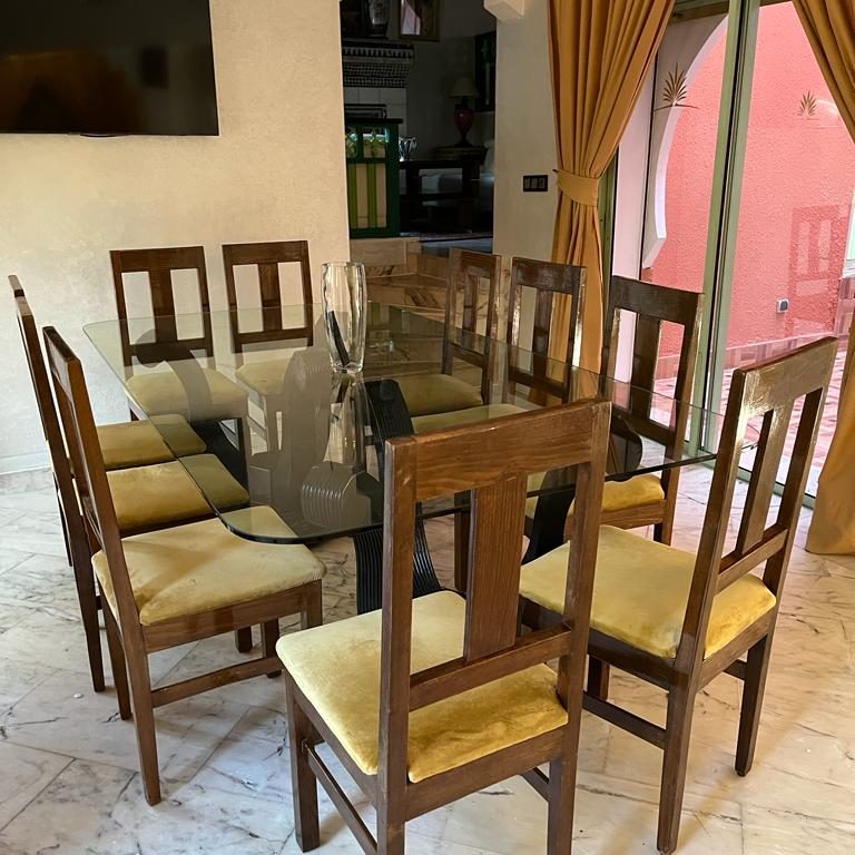 A spacious dining table with eight wooden chairs and a glass top in a well-lit room.