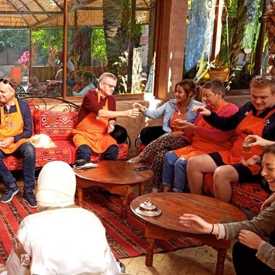 A group of people in orange aprons enjoying a workshop in a lively, sunny setting.