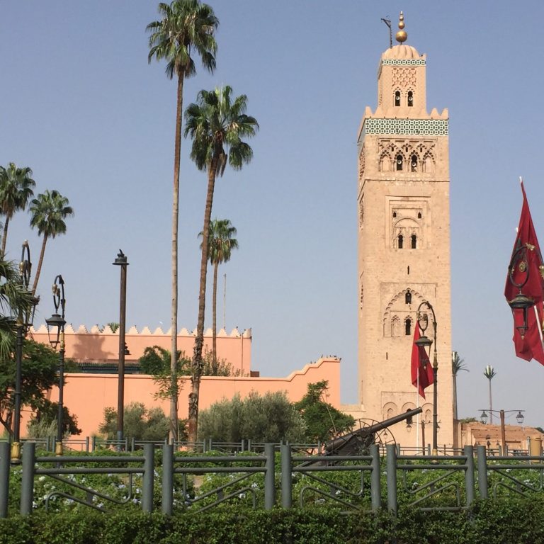 Koutoubia Mosque tower with palm trees and Moroccan flags in a sunny setting.