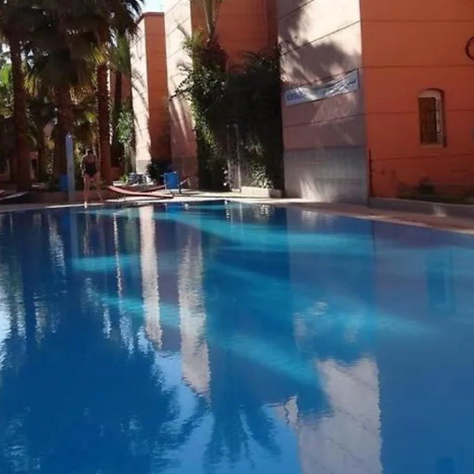 Serene outdoor swimming pool surrounded by palm trees and orange buildings.