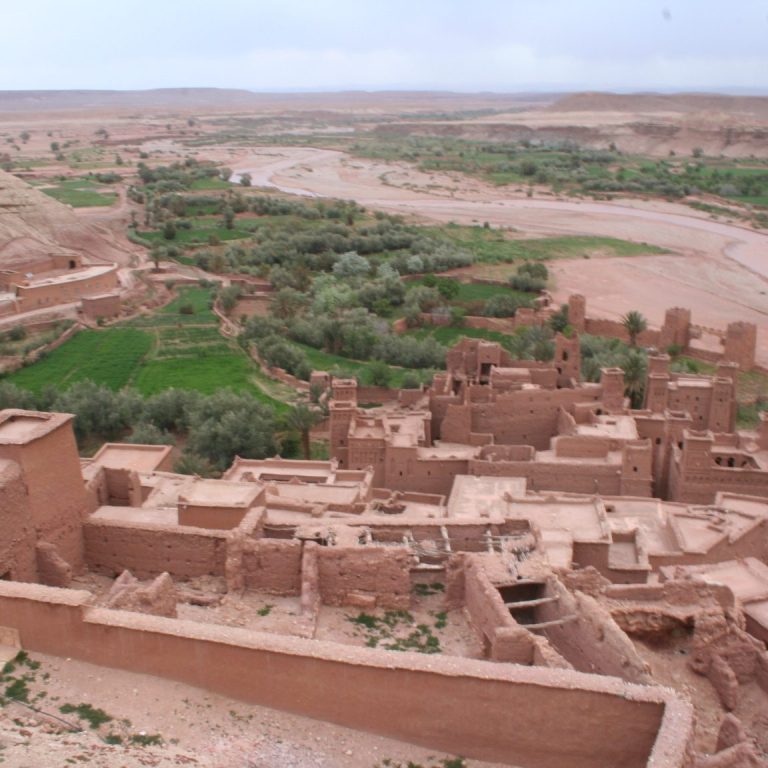 Ancient earthen ruins on a hillside overlooking a green valley and river.
