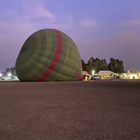 A green hot air balloon with red stripes on a gravel surface at dusk.