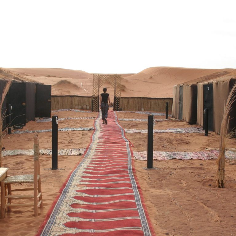 A winding red carpet leads through a desert camp with tents and seating areas.