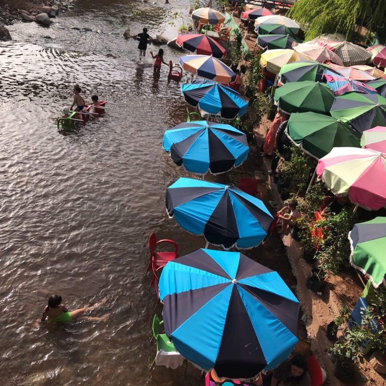 People enjoying a river with colourful umbrellas providing shade along the banks.